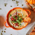 cauliflower pumpkin soup in orange bowl beside roasted garlic, pepitas, toasted baguette, pumpkins