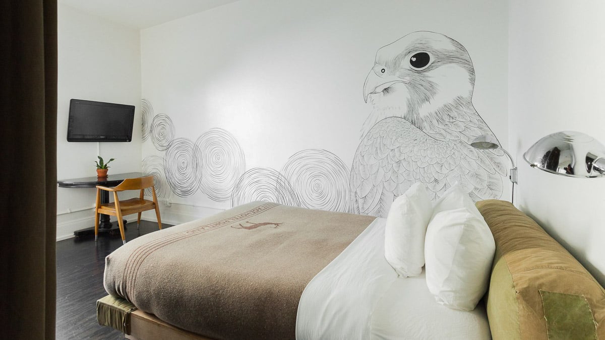 Ace Hotel bedroom with modern decor, flat screen tv, and bird mural on the wall