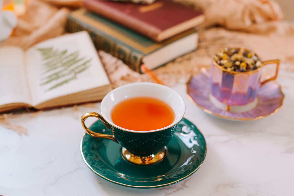 green teacup full of juniper berry tea surrounded by books, purple teacup