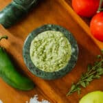 jalapeno pesto (spicy pesto) in a mortar alongside pesto ingredients and tomatoes