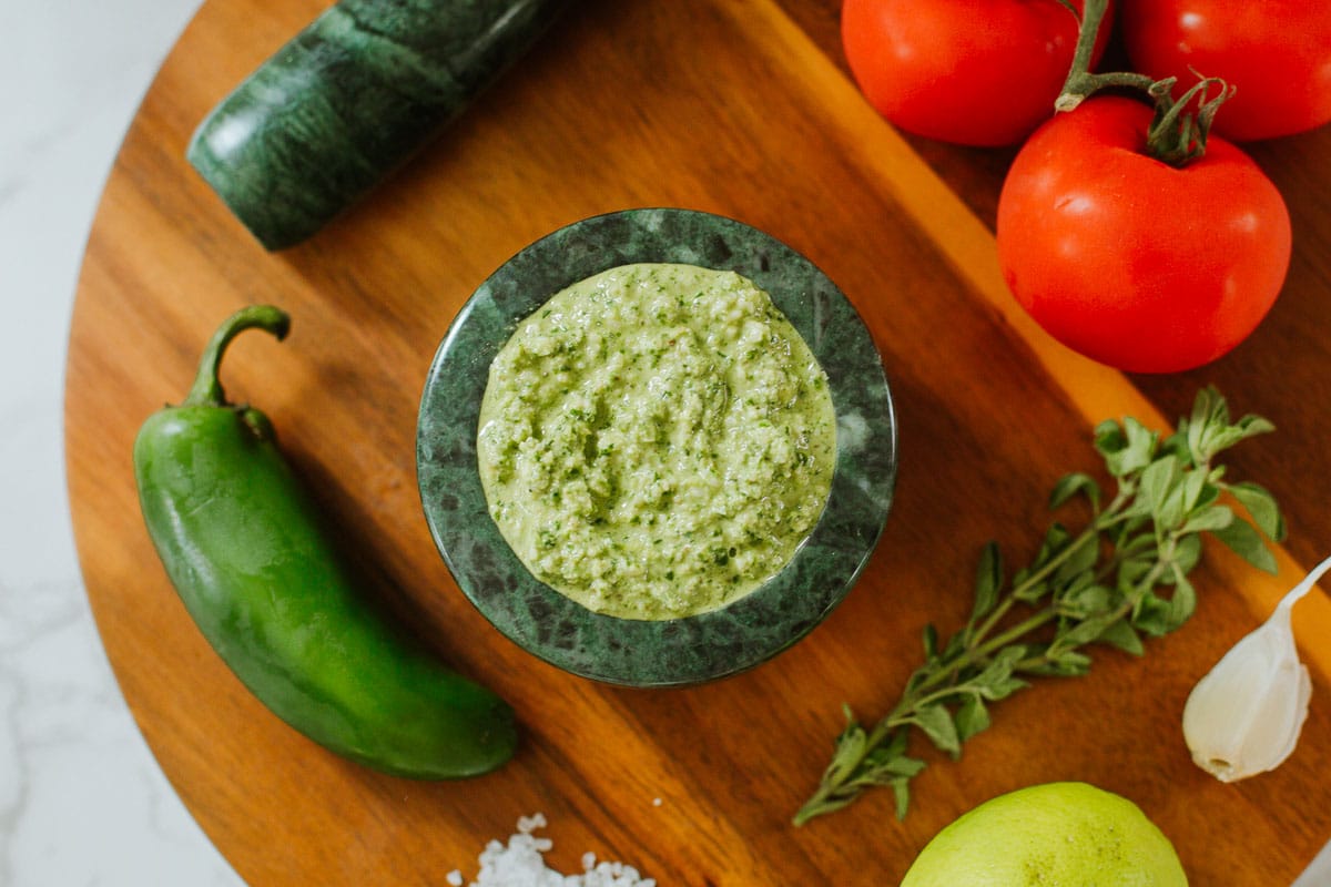 jalapeno pesto (spicy pesto) in a mortar alongside pesto ingredients and tomatoes