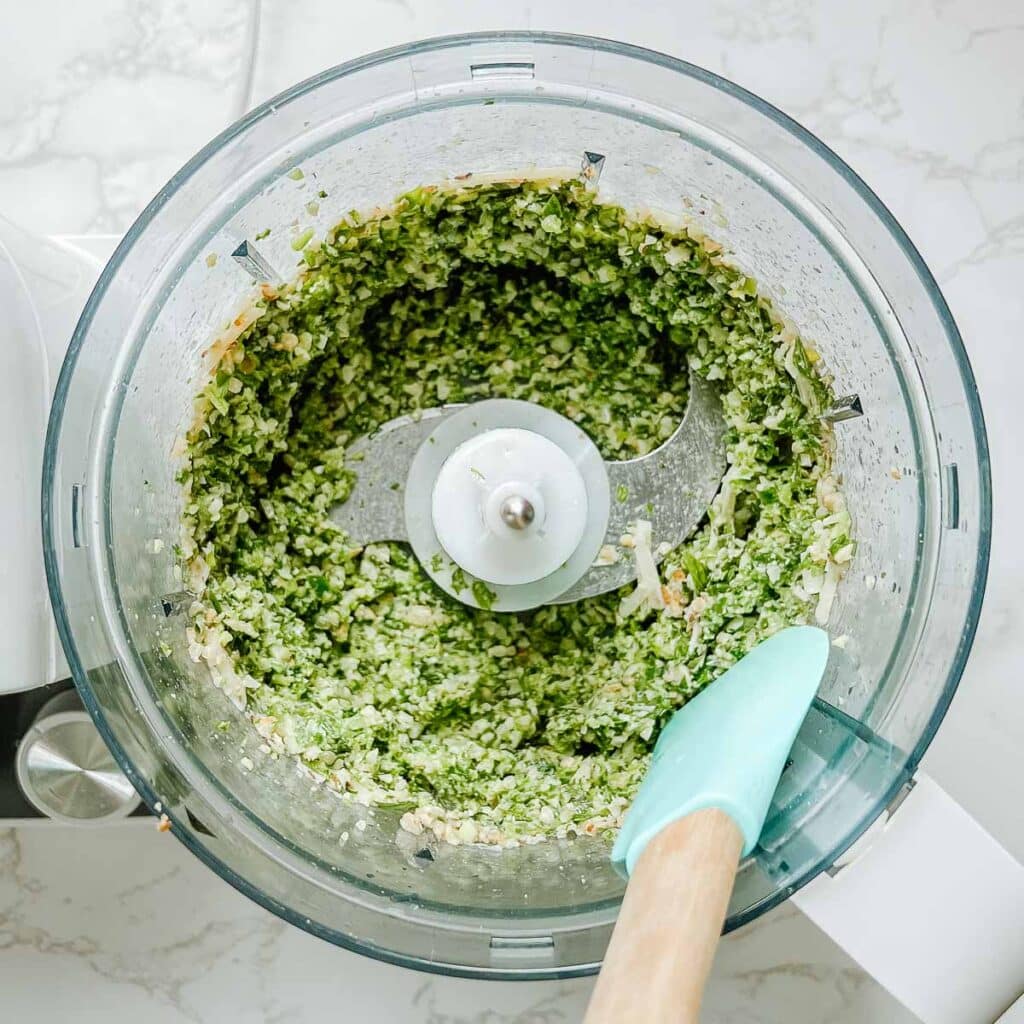 rubber spatula scraping food processor edges after blending pesto
