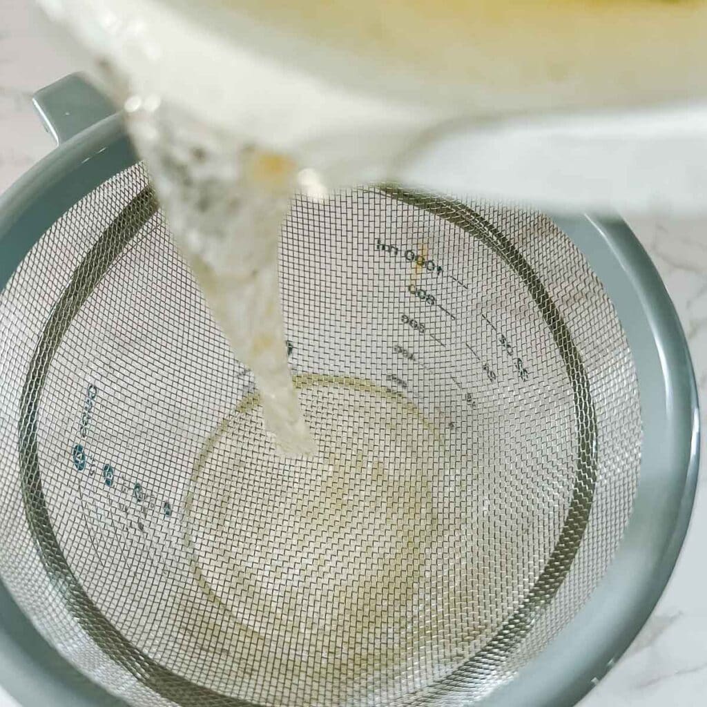 rosemary water for hair growth being poured through strainer