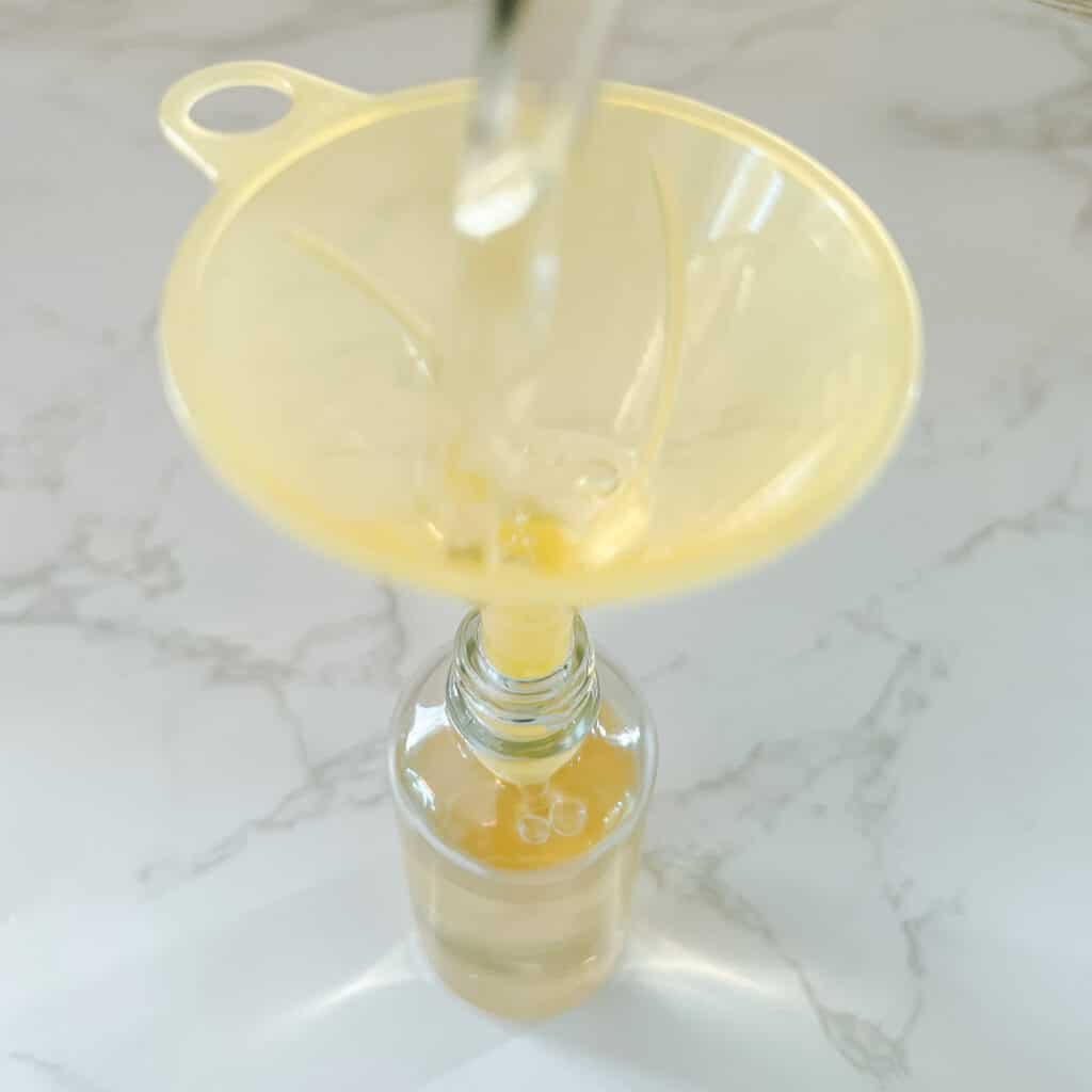 rosemary water beinf poured through funnel into glass bottle