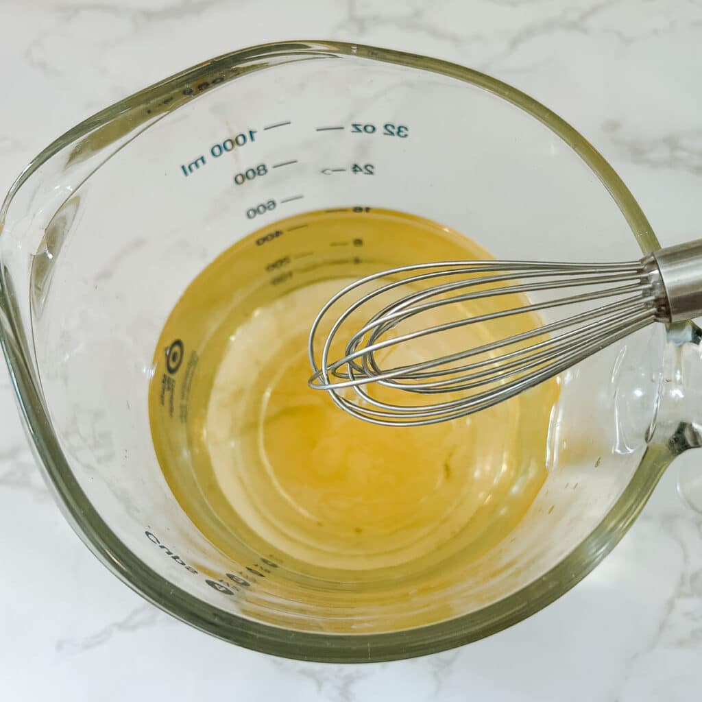 whisk over measuring cup full of rosemary water for hair growth