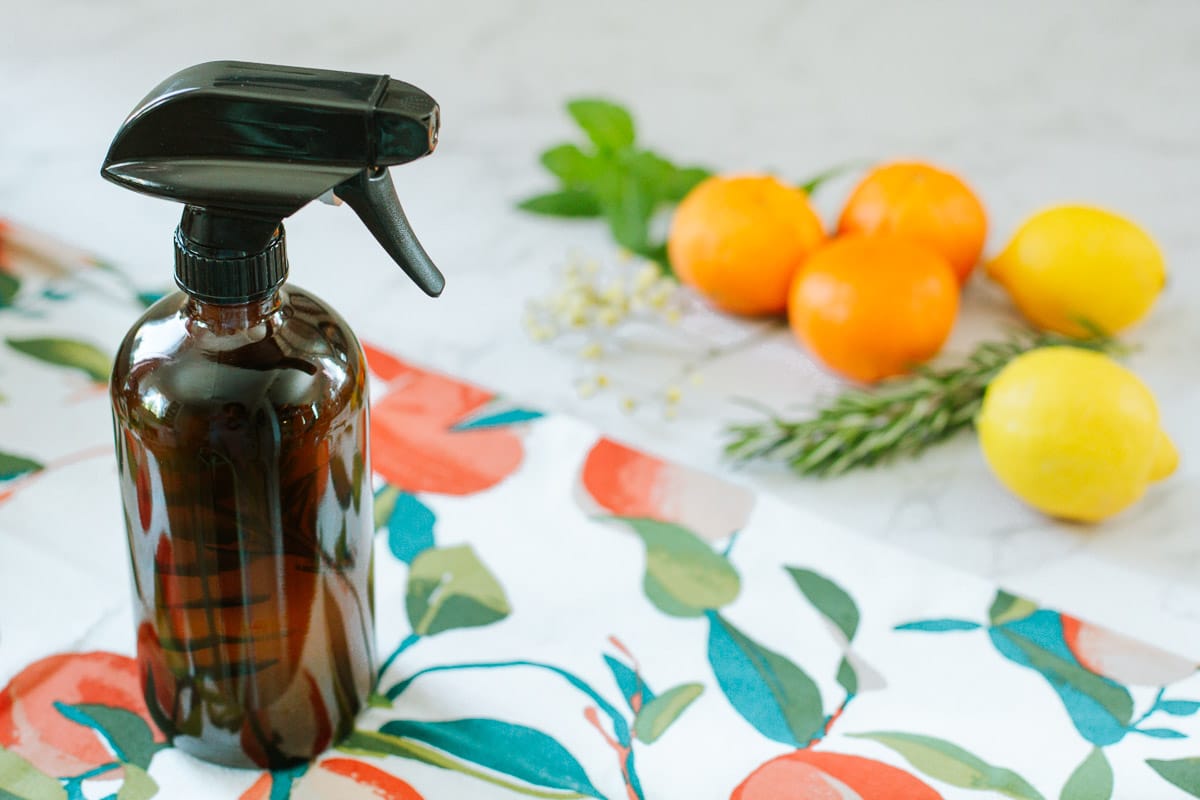 orange peel & vinegar cleaner in spray bottle beside colorful towel, fruits, herbs