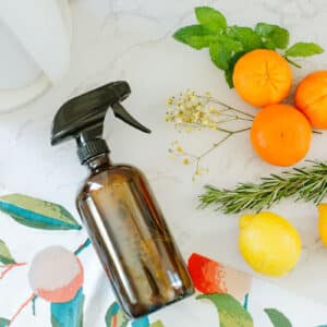 orange peel & vinegar cleaner in spray bottle beside colorful towel, fruits, herbs, paper towels