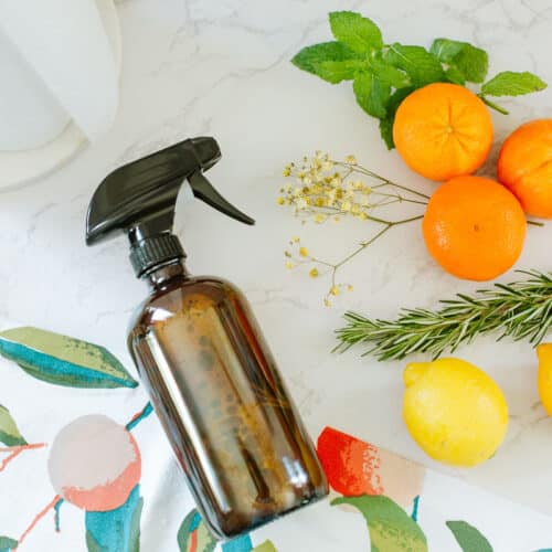 orange peel & vinegar cleaner in spray bottle beside colorful towel, fruits, herbs, paper towels