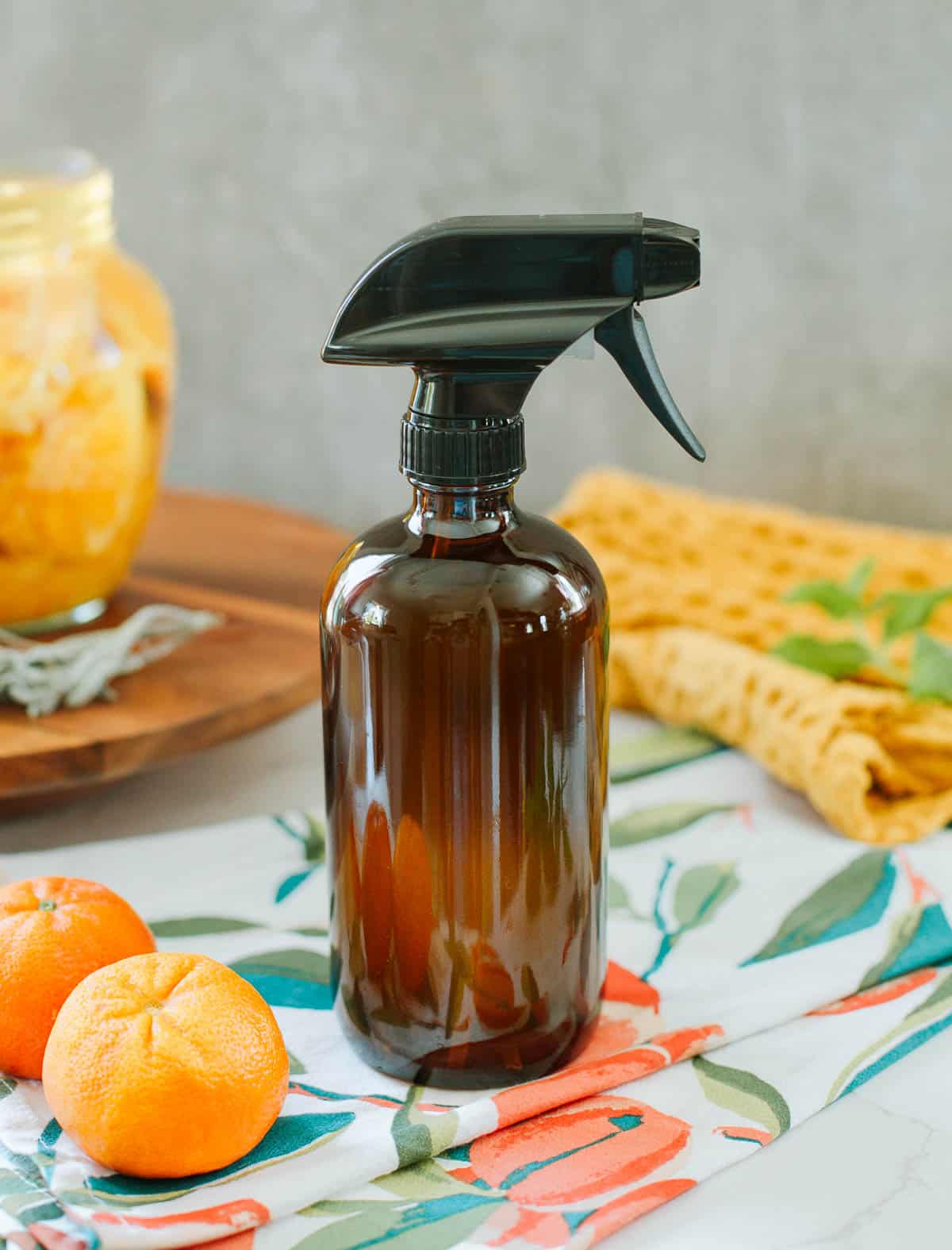 orange peel & vinegar cleaner in spray bottle beside colorful towels, fruits, herbs, jar of peels