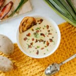 Cauliflower potato leek soup with crusty bread beside ingredients