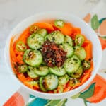 bowl of carrot and cucumber salad with heap of chili crisp on top
