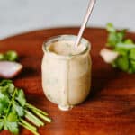 chimichurri aioli dripping from jar on cutting board beside fresh herbs.