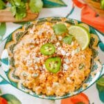 jalapeño creamed corn in bowl beside cilantro and jalapeno on patterned background.