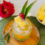 pineapple skin tea in tumbler with ice and fruit skewer beside flowers and pineapple chunks in bowl.