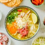 loaded pork pozole verde surrounded by cilantro, radish, onion, cabbage, carrots, tortillas.