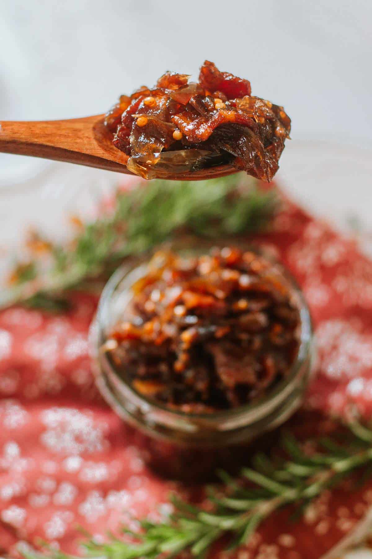 heaping spoonful of caramelized onion jam with bacon above mason jar full of jam beside rosemary sprigs.