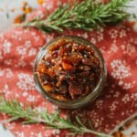 caramelized onion jam in mason jar on floral placemat with fresh rosemary sprigs.