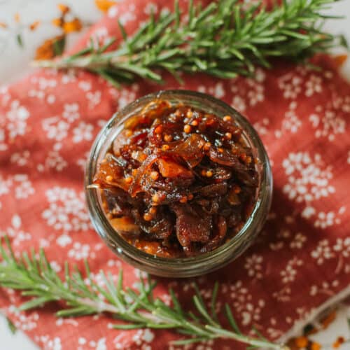 caramelized onion jam in mason jar on floral placemat with fresh rosemary sprigs.