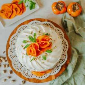 persimmon cake topped with persimmon slices formed into "roses" beside fresh fuyu persimmons, pistachios, and tea towel.