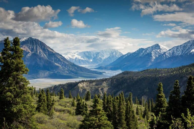 A scenic view of majestic mountains under a partly cloudy sky, with lush greenery in the foreground.