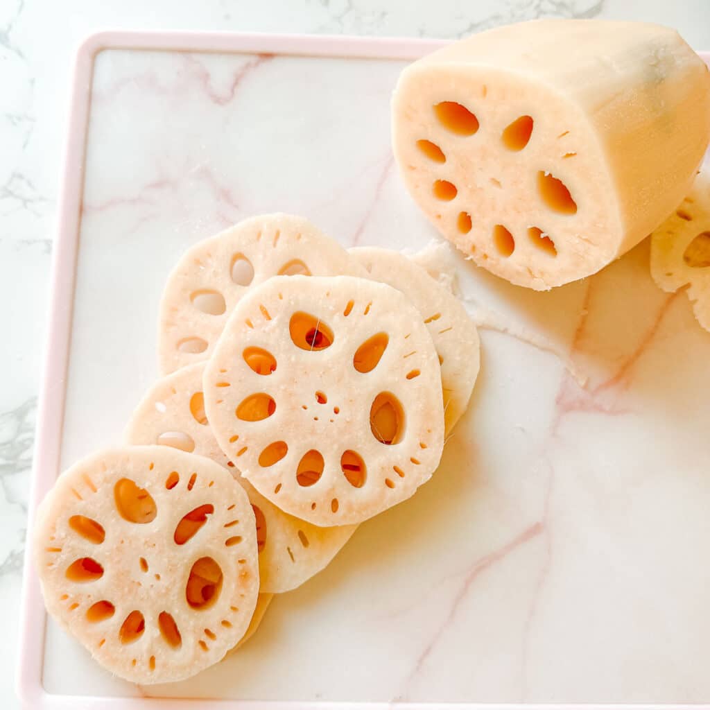 thick lotus root slices on cutting board beside whole lotus root.