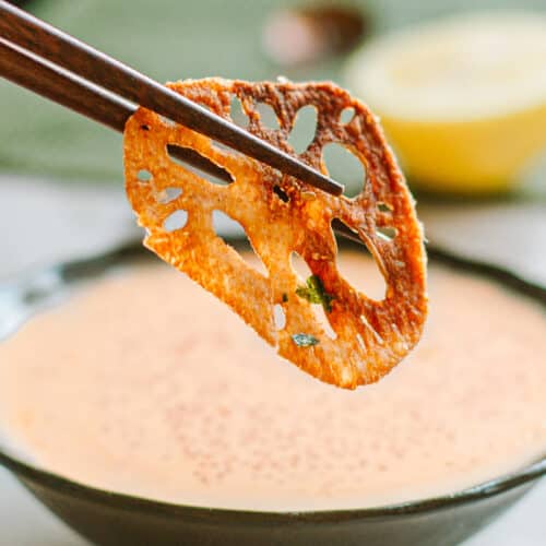 lotus root chip being dipped in masago sauce with chopsticks.
