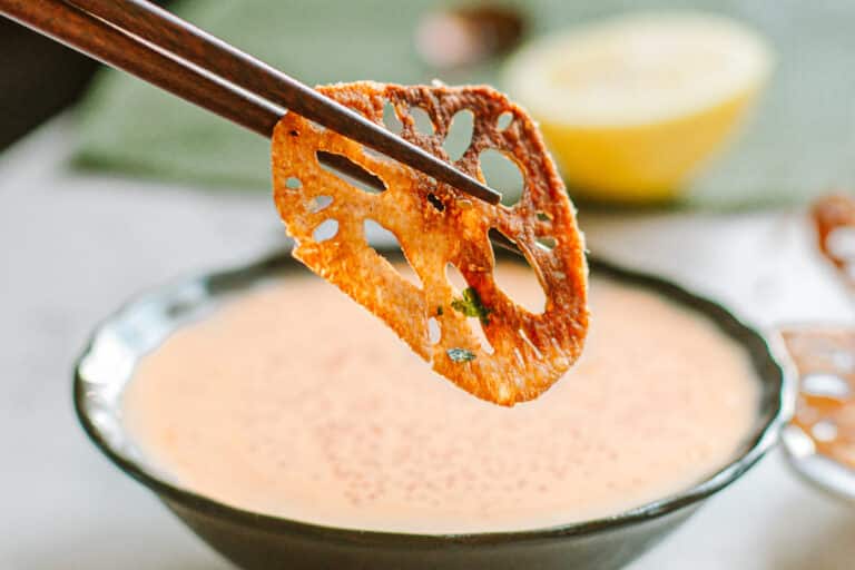 lotus root chip being dipped in masago sauce with chopsticks.