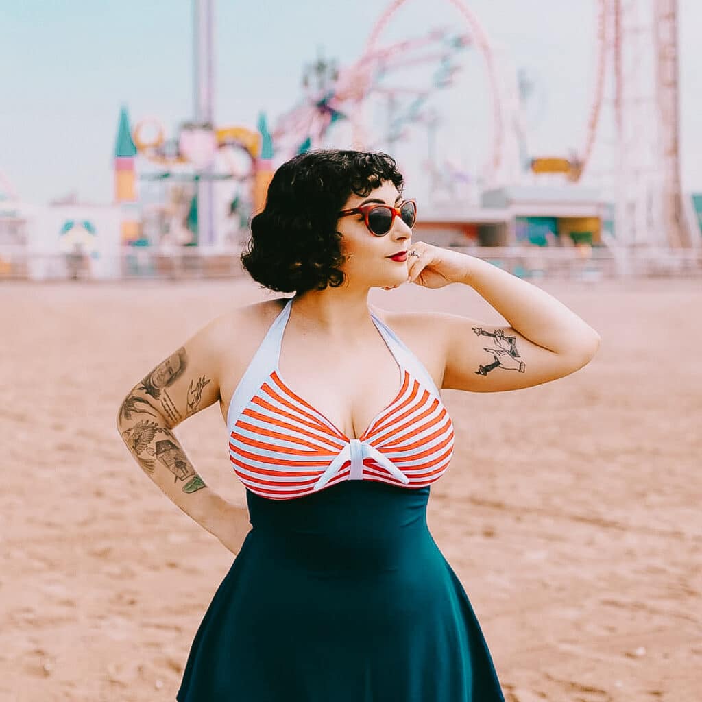 me standing on the beach in a striped swimsuit at Coney Island with park rides in background.