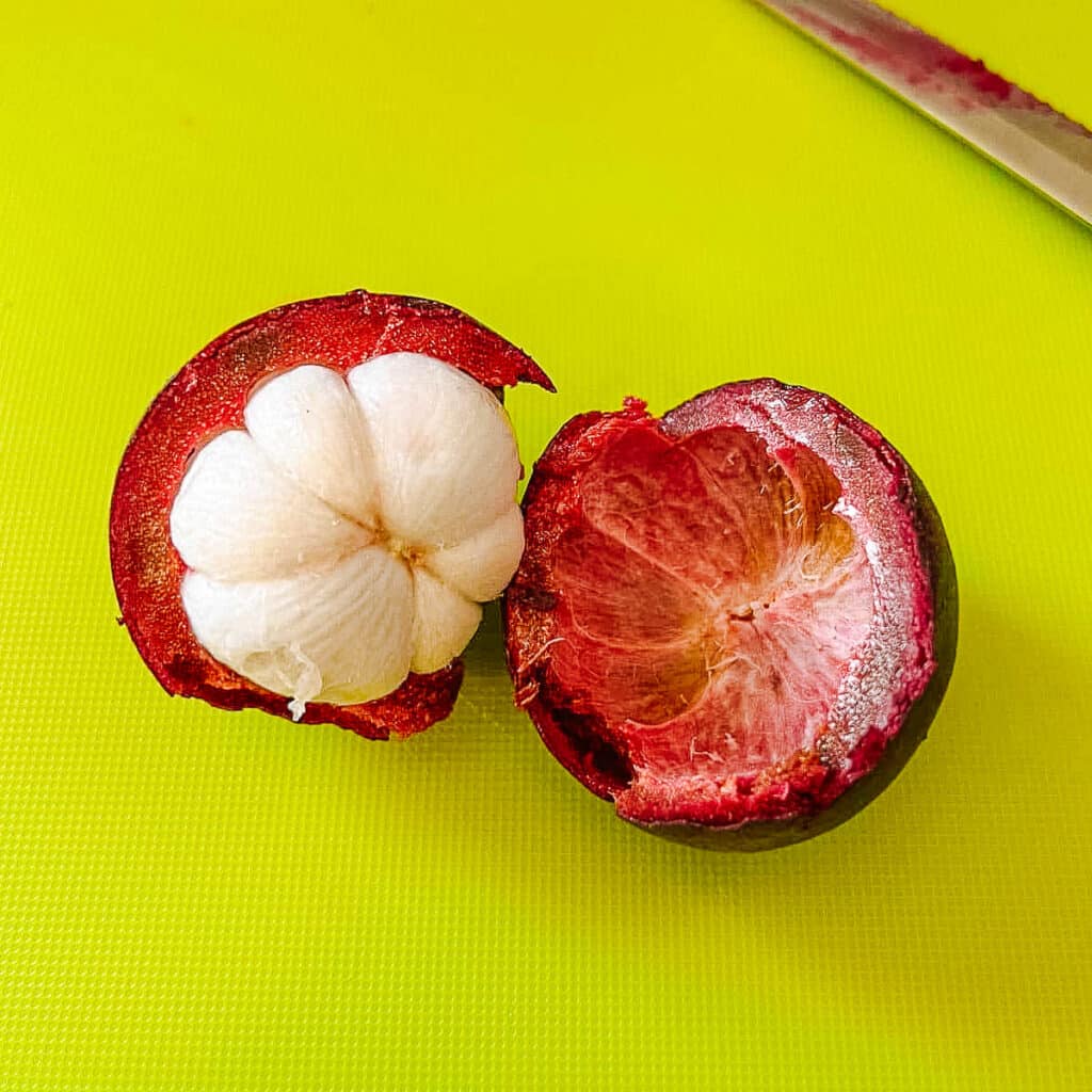 mangosteen after halving the rind and exposing the while flesh beside serrated knife.