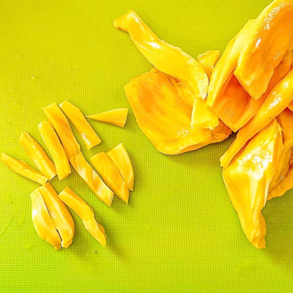 sliced jackfruit beside whole jackfruit on cutting board.