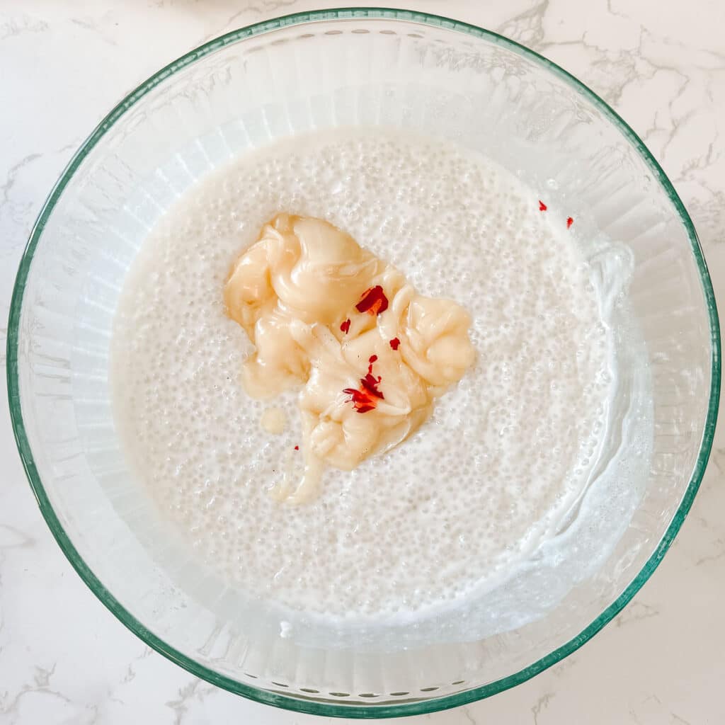 condensed coconut milk and red food coloring in coconut milk sago before stirring.